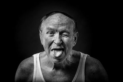 Portrait of man winking while sticking out tongue against black background