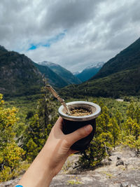 Cropped hand of woman holding drink against mountain