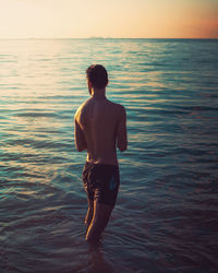 Rear view of shirtless man standing in sea against sky