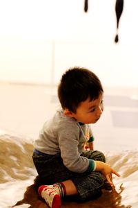 Cute boy sitting on bed at home