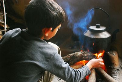 Boy preparing chai in kettle on fire
