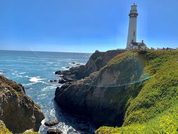 Lighthouse by sea against clear sky