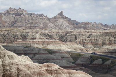 A truck drives through surreal badlands formations against cloudy, hazy sky.