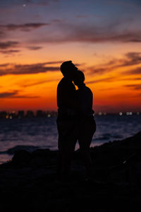 Silhouette of a couple standing by sea against sky during sunset huging esch other