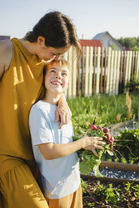 Happy mother embracing smiling son holding radish at garden