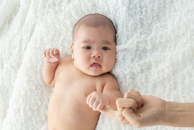 Cropped image of mother holding baby daughter hand lying on bed