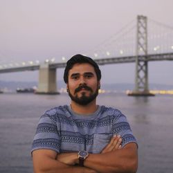 Portrait of man with arms crossed standing against bay bridge