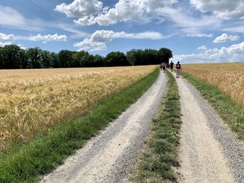 Dirt road amidst agricultural field against sky
