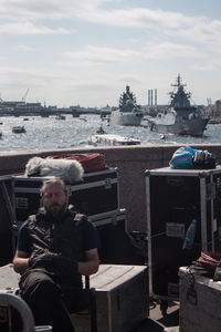 Man sitting at commercial dock against sky