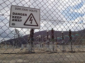 Information sign on chainlink fence against sky