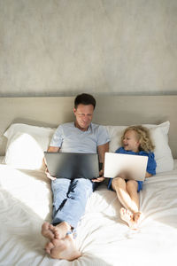 Happy girl and father with laptops on bed in bedroom