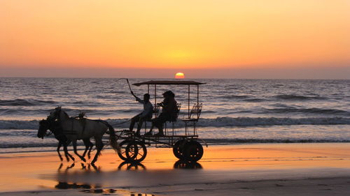 Side view of silhouette horse ride on beach at sunset