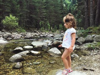 Cute girl standing on rock at lakeshore in forest