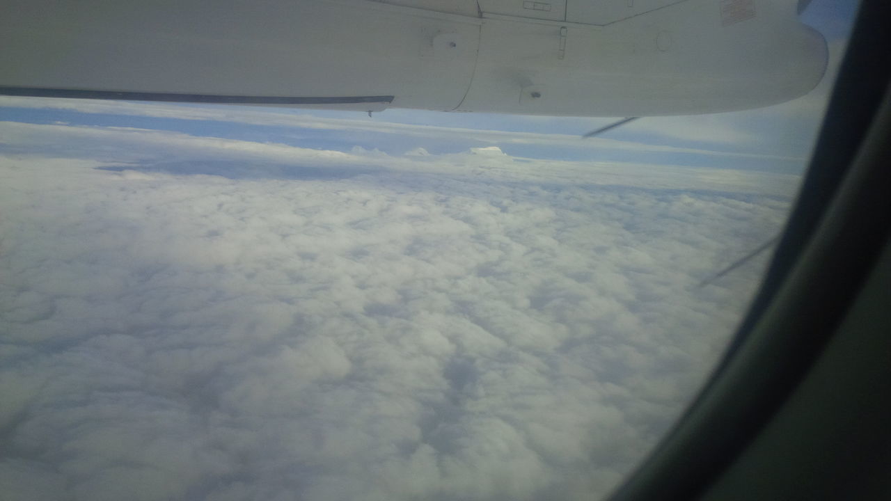 CROPPED IMAGE OF AIRPLANE FLYING OVER CLOUDS SEEN THROUGH WINDOW