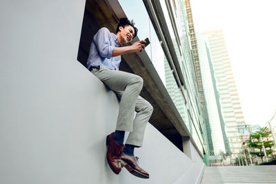 Side view of young man photographing against sky in city