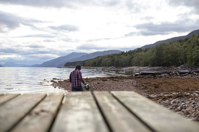 A man walks in the distance along the shore carrying a crab pot