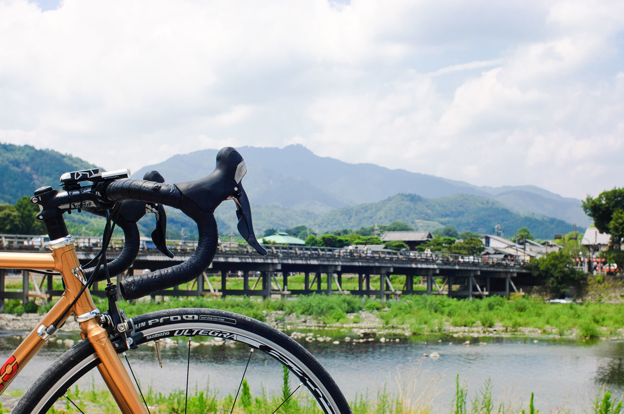 mountain, transportation, mountain range, sky, mode of transport, water, river, cloud - sky, land vehicle, lake, tranquility, bicycle, nature, scenics, bridge - man made structure, railing, cloud, beauty in nature, tranquil scene, day