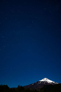 Low angle scenic view of star field over mountain against blue sky during winter