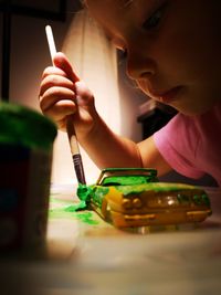 Close-up of cute mischievous girl painting toy car at home