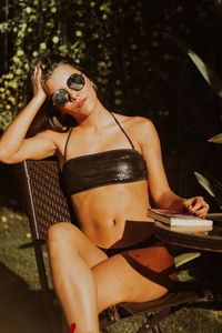 Sensuous woman sitting with book at table against trees