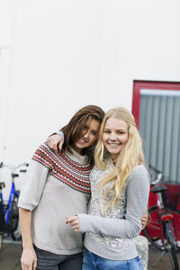 Portrait of happy teenage girls standing arm around on high school campus