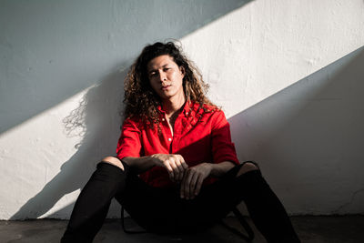 Portrait of beautiful young woman sitting against wall