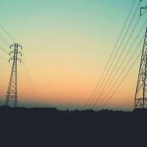 Low angle view of silhouette electricity pylons against clear sky