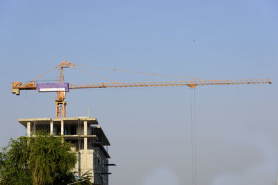 Low angle view of crane by building against sky