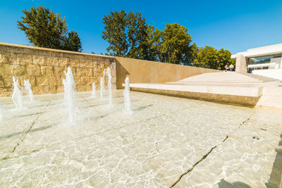 Fountain by swimming pool against sky on sunny day