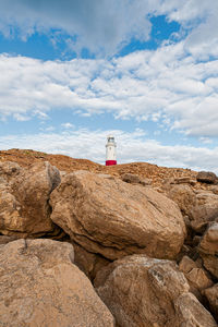 Lighthouse on rock by building against sky