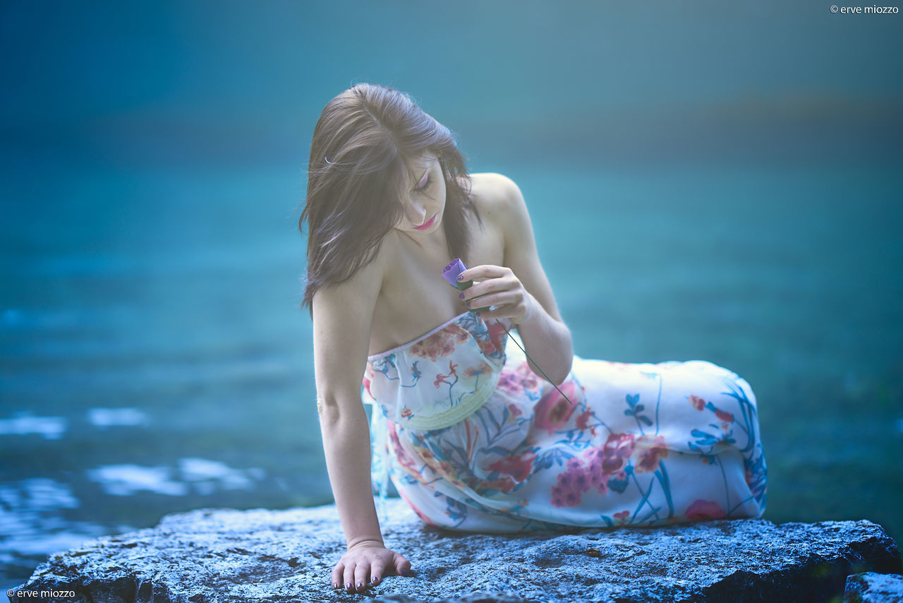 women, water, blond hair, blue, one person, nature, adult, clothing, hairstyle, sea, long hair, young adult, fashion, land, full length, dress, child, female, summer, photo shoot, beach, sitting, childhood, emotion, relaxation, vacation, outdoors, trip, rock, holiday, beauty in nature, person, day, looking, portrait photography, romance, leisure activity, tranquility, sky, environment, lifestyles, cute