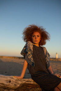 Portrait of smiling young woman standing at beach against clear sky