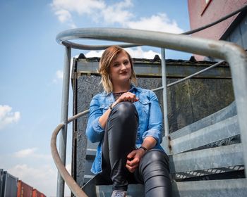 Portrait of smiling woman sitting staircase against sky