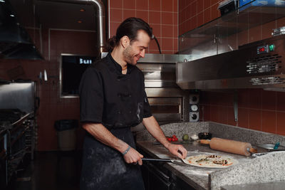 Side view of male shed  working in kitchen making a pizza