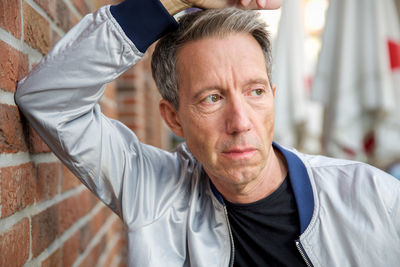 Close-up of thoughtful man standing by brick wall