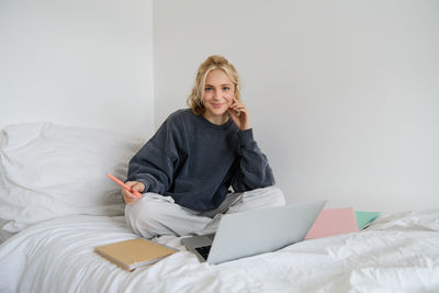 Young woman using laptop while sitting on bed at home