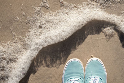 Tip of canvas shoes covered feet standing on sand framed by sea foam