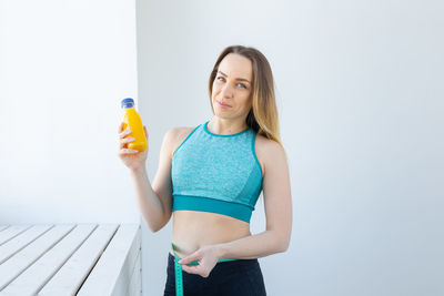 Portrait of young woman holding bottle while standing against white background