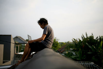 Side view of young man sitting and working at rooftop