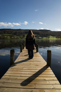 Rear view of mature woman standing on pier over lake