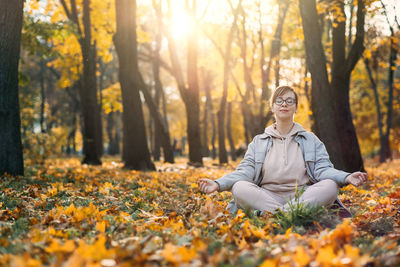 Caucasian middle aged woman meditating in lotus pose at autumn park with sunlight. yoga at fall