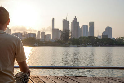 Rear view of man looking at river by city buildings