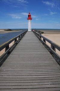 Pier leading towards lighthouse by sea against sky