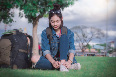 Woman tying shoelace while sitting on field