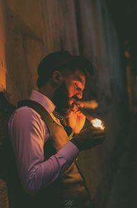 Man smoking cigar while standing by wall at night