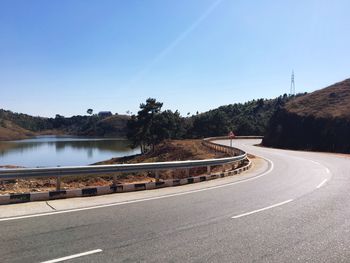 Road by lake against clear blue sky