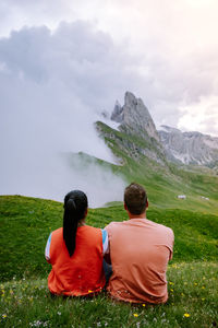 Rear view of couple sitting on mountain against sky