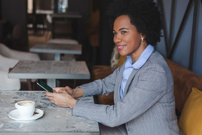 Side view of businesswoman using mobile phone while sitting in cafe