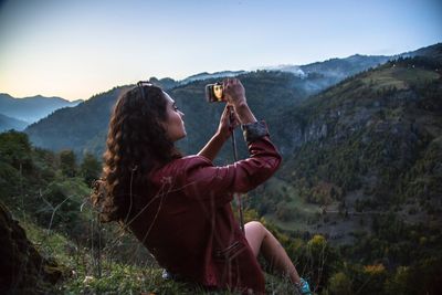 Young woman photographing while sitting on mountain