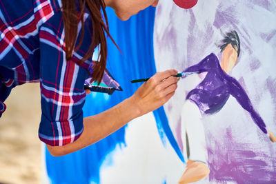 Female artist painting on wooden canvas board at outdoor festival, young adult painting picture